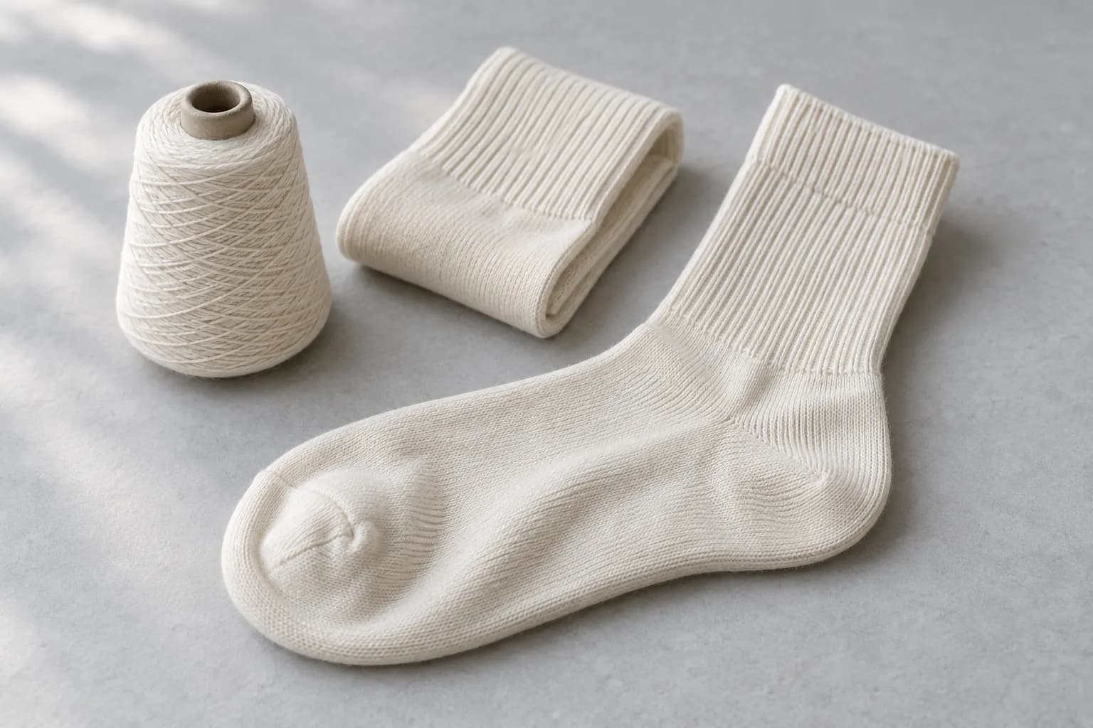 Illustrative ivory crew socks beside a single matching yarn cone